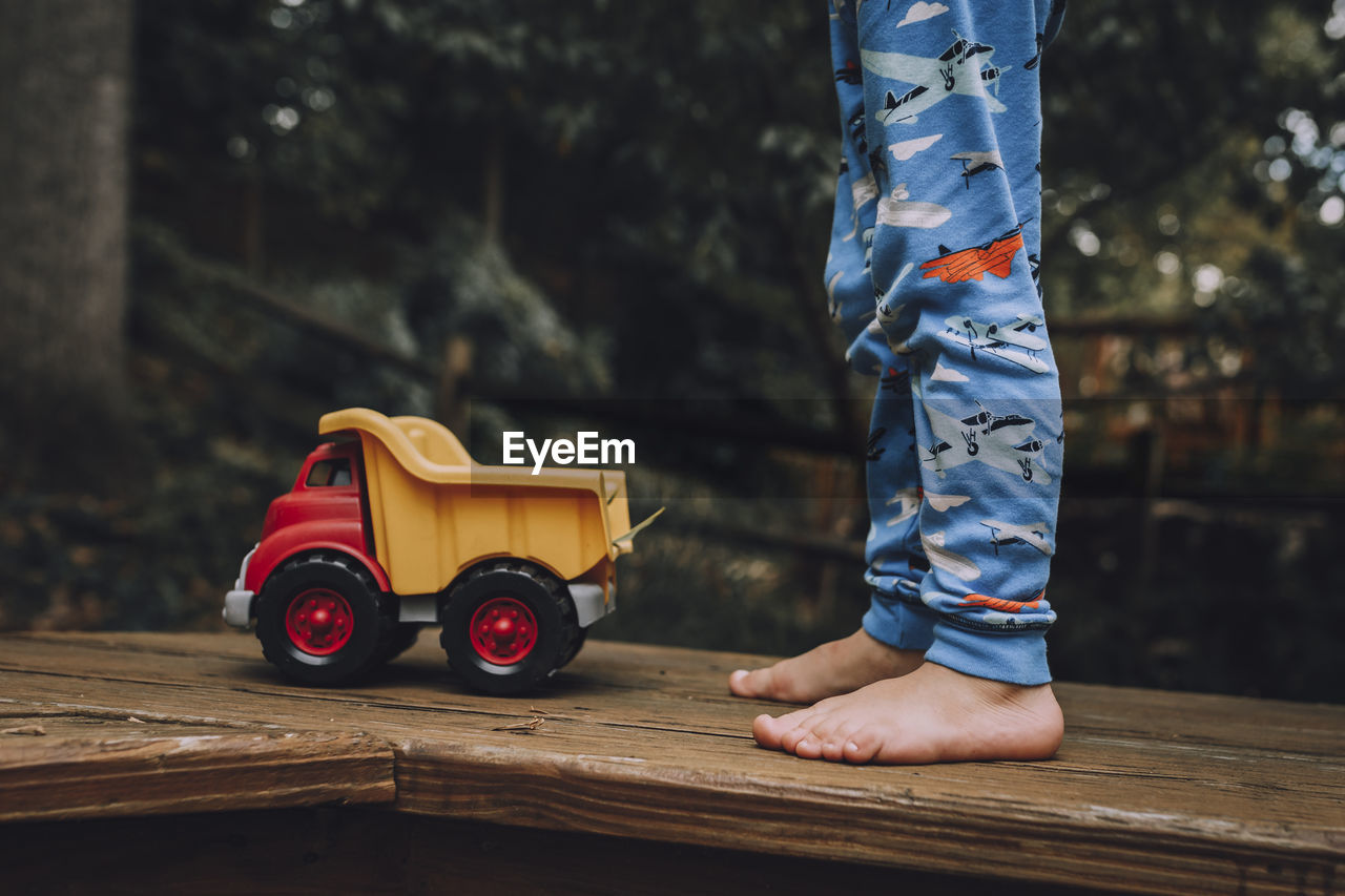 Low section of child standing by toy car on wooden floor