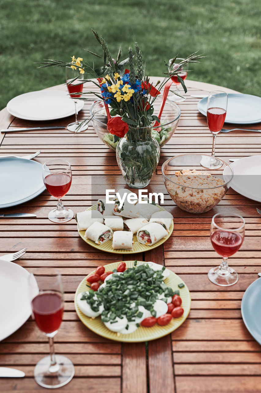 Dinner in an apple orchard garden on wooden table with salads and wine decorated with flowers