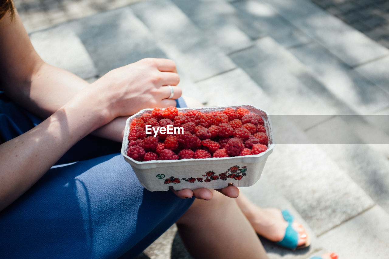 Low section of woman holding raspberries box while sitting on steps