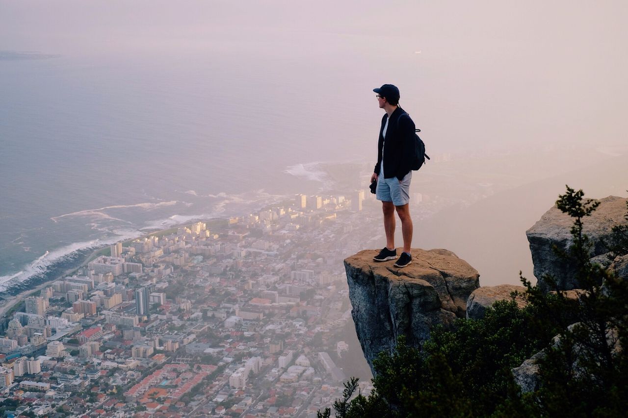 Man standing on rock at mountain peak looking at cityscape and sea