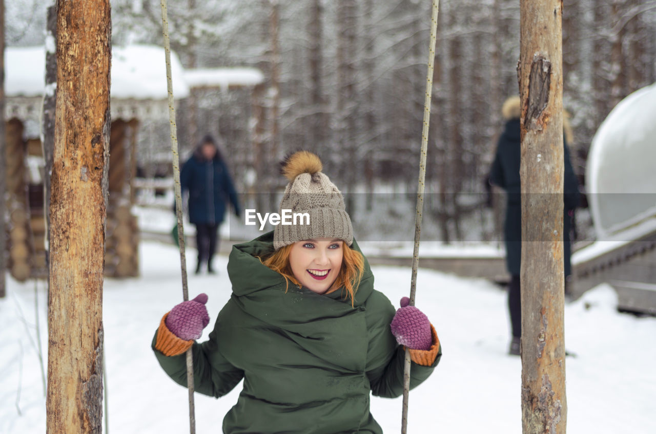Woman sitting on swing on snow covered field during winter