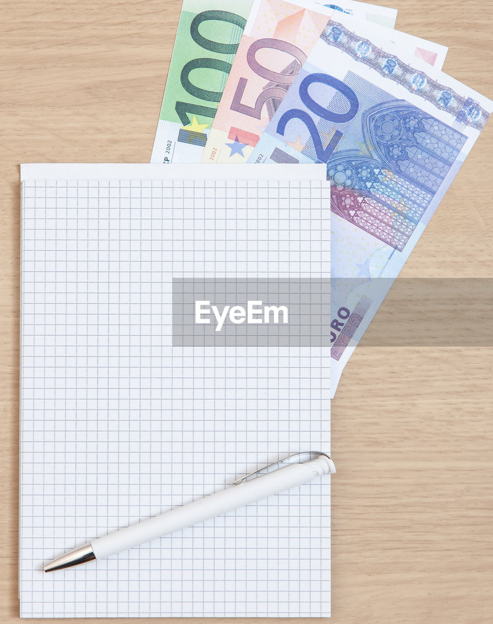 High angle view of pen and note pad with various euro notes on table