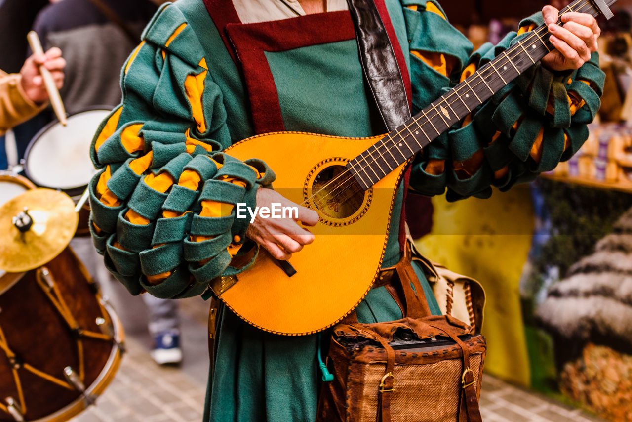 Midsection of man wearing traditional clothing while playing string instrument on road during parade
