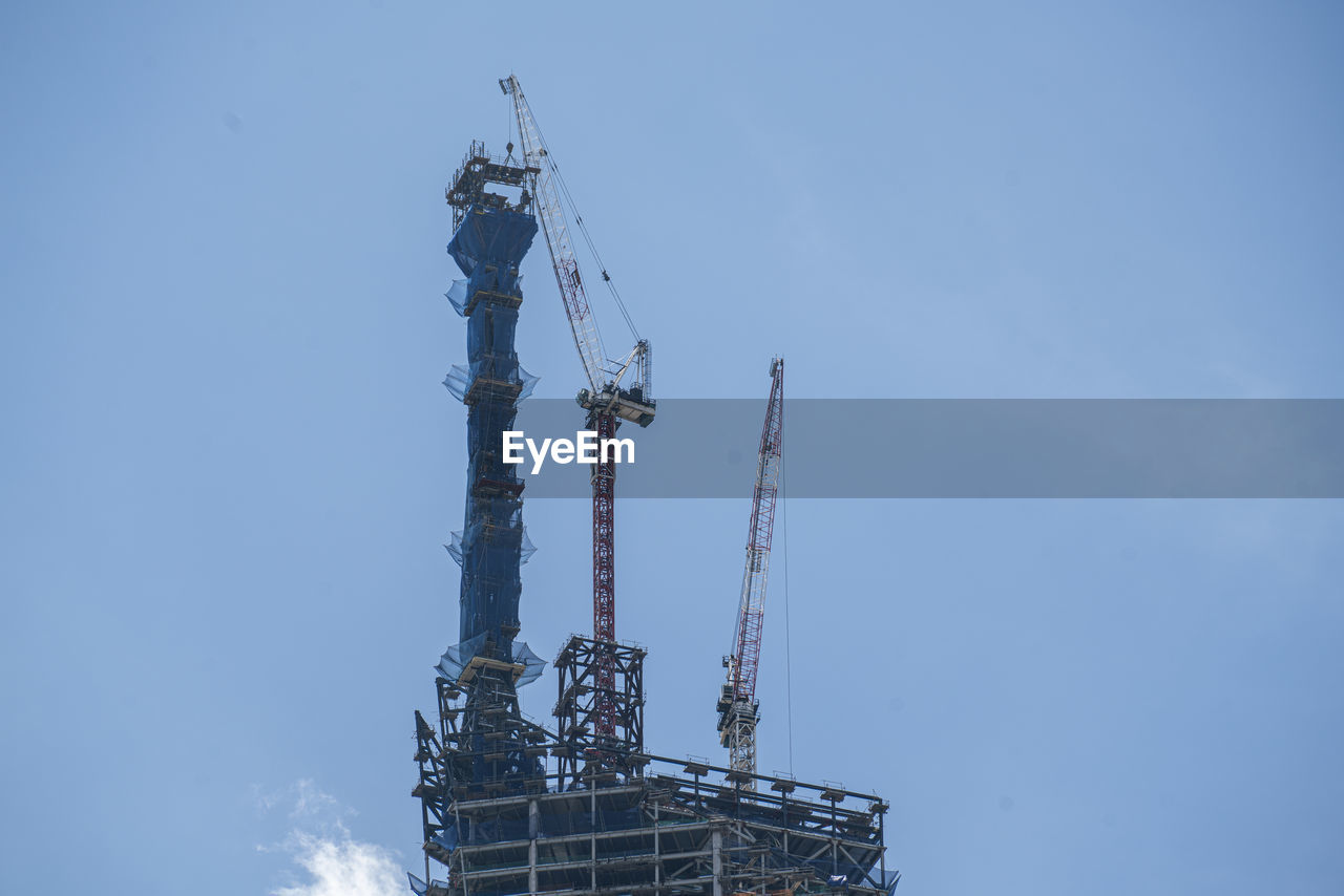 LOW ANGLE VIEW OF CRANES AGAINST BLUE SKY
