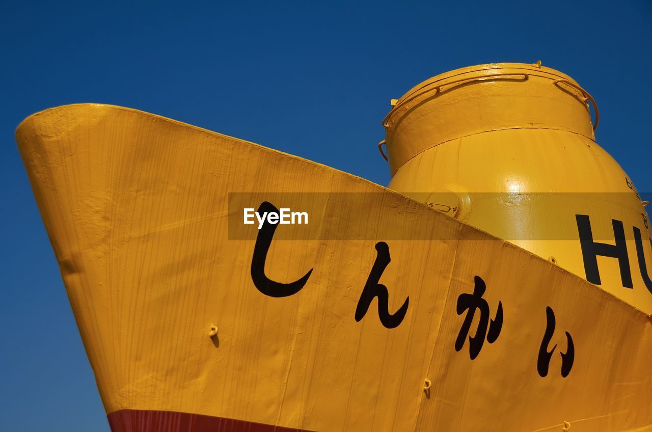 Low angle view of japanese text on yellow submarine against clear sky