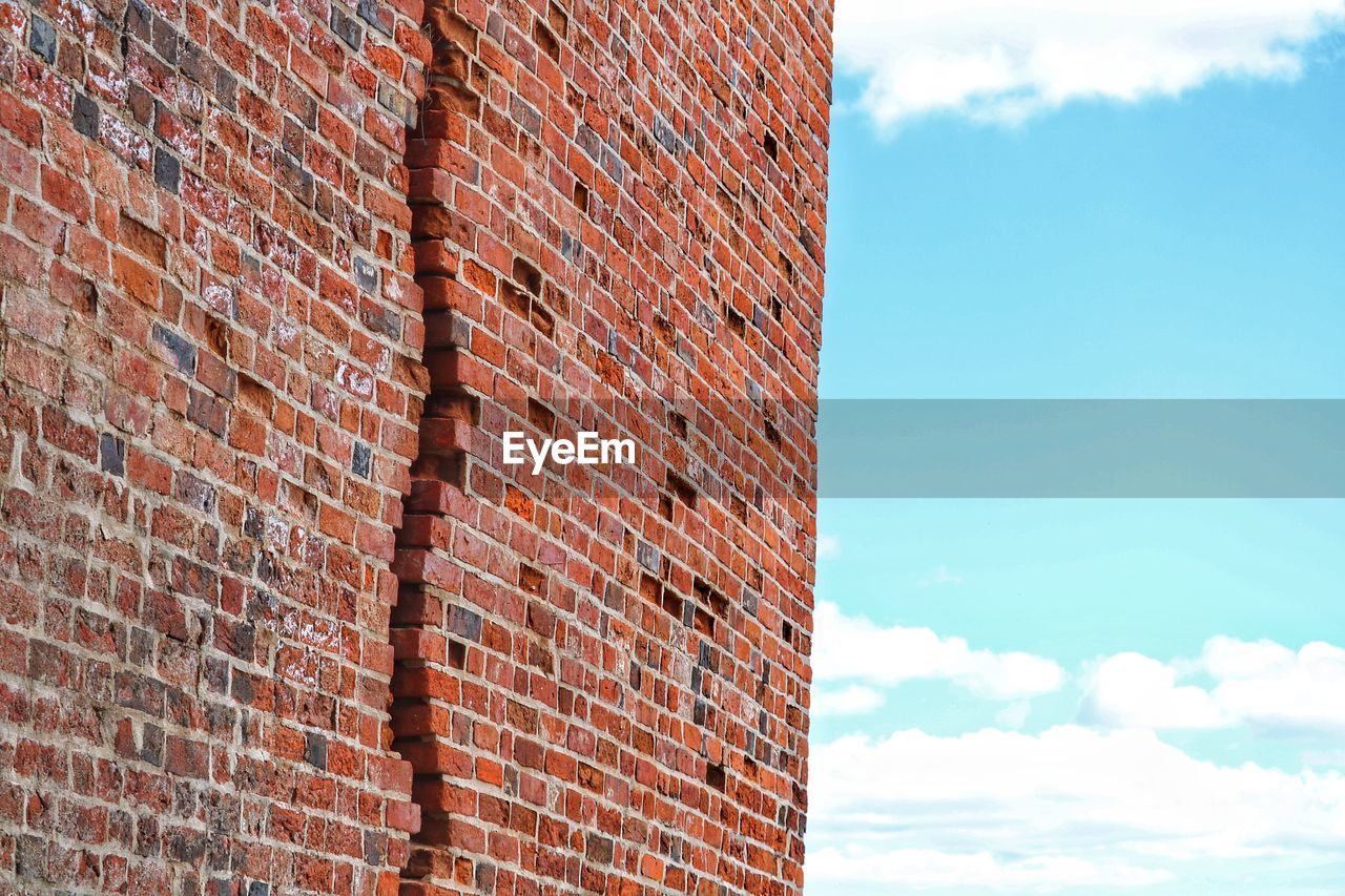 LOW ANGLE VIEW OF BRICK WALL AND BUILDING AGAINST SKY