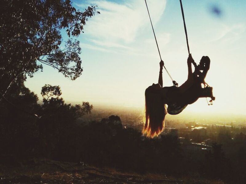 Low angle view of girls swinging in park during sunset