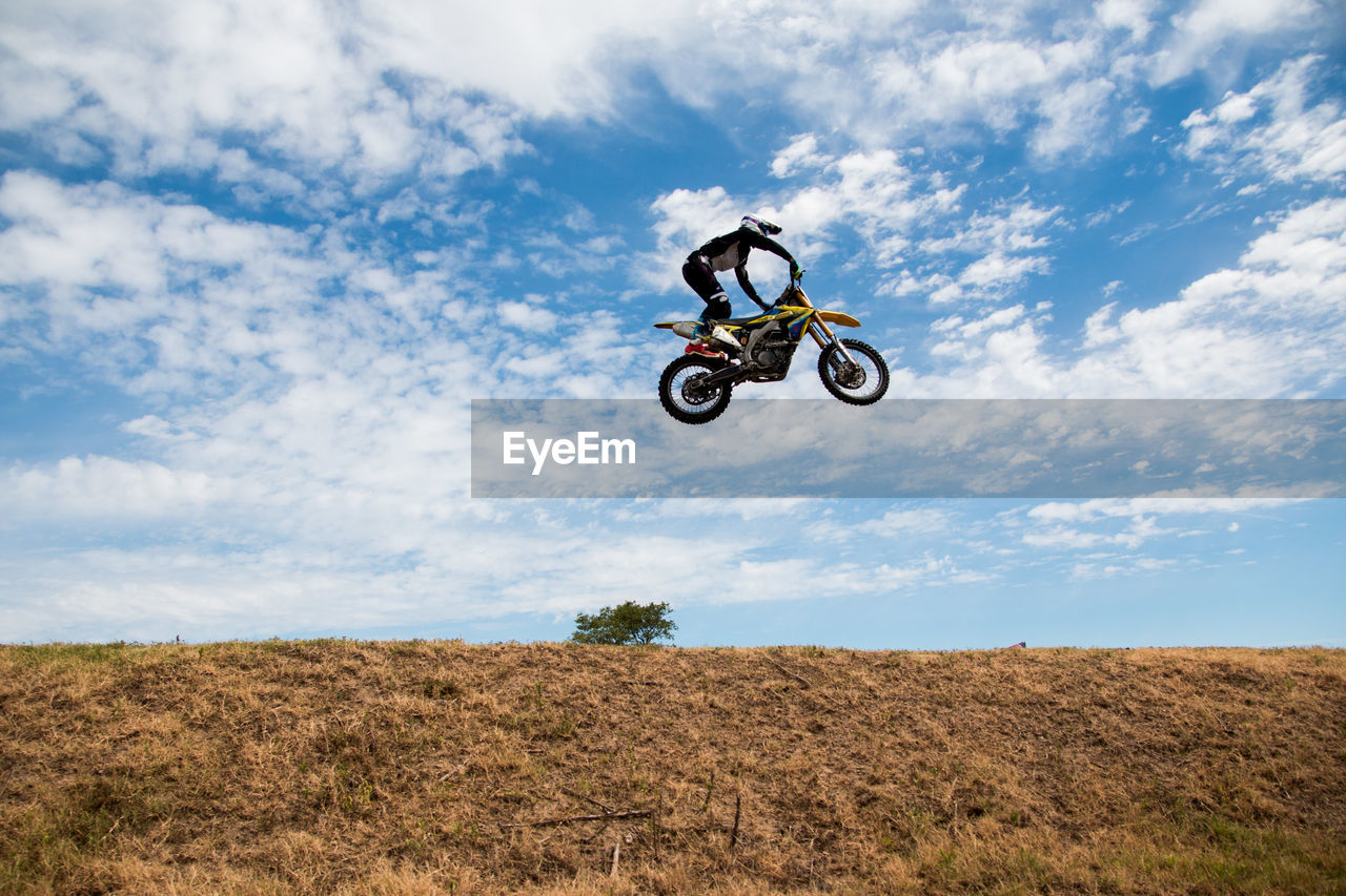Low angle view of man jumping motorcycle over field against cloudy sky