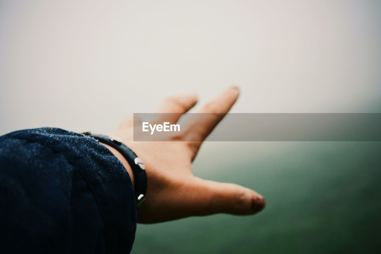 Cropped image of person hand against sky during foggy weather