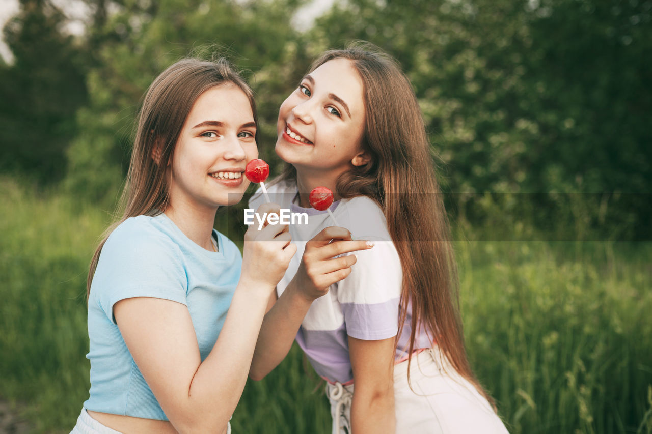 Portrait of smiling friends holding lollipops standing against plants in park