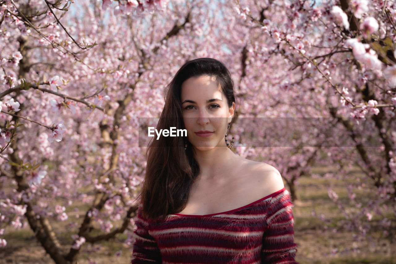 Portrait of beautiful young woman standing by cherry blossom tree