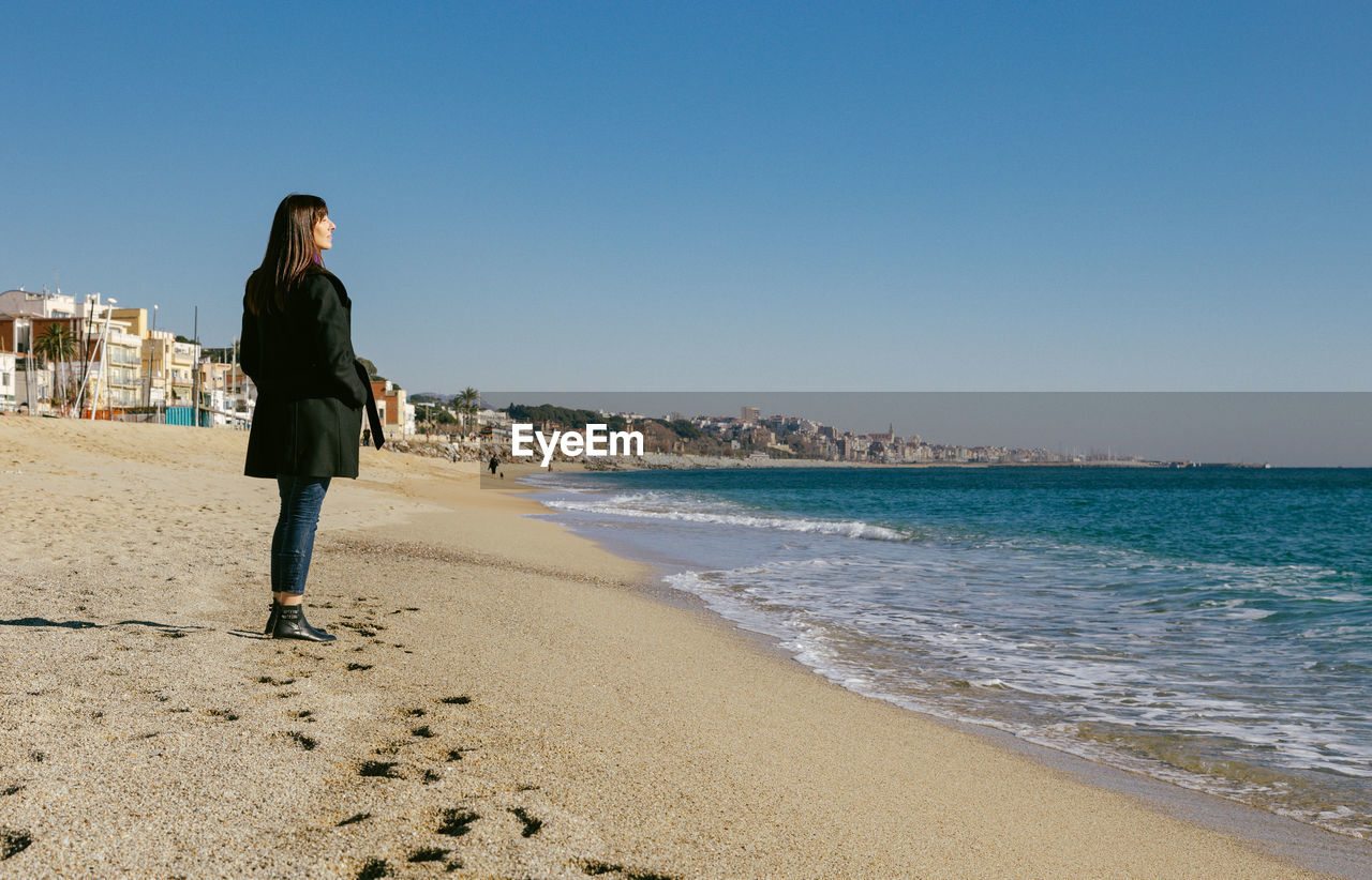 Middle-aged woman standing on the beach looking at the sea on a sunny winter day