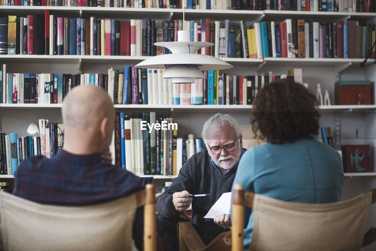 Senior therapist explaining analysis to mature couple against bookshelf at home office