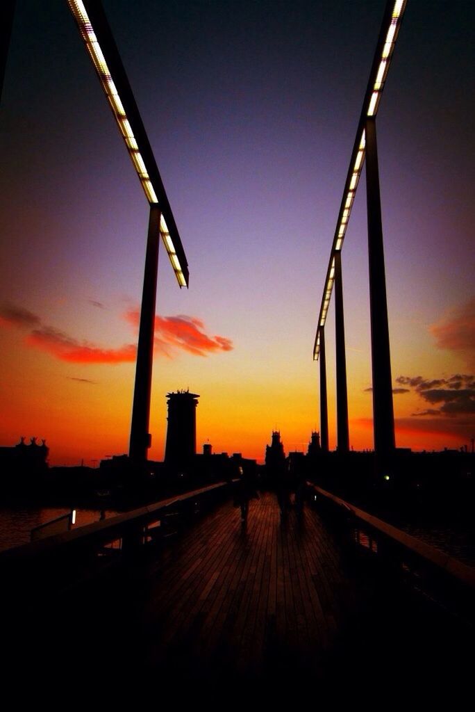 Bridge leading towards silhouette buildings at sunset