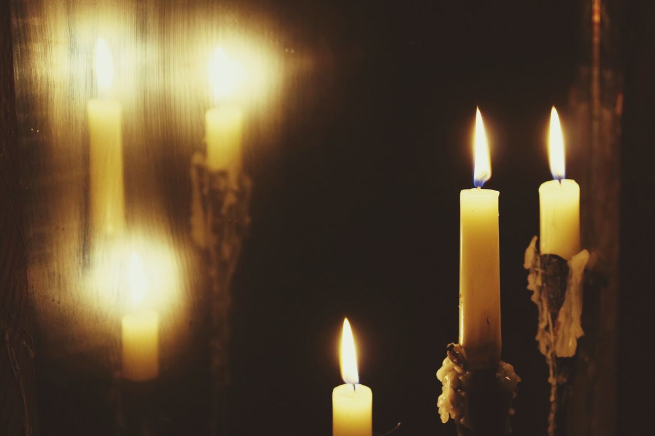 Close-up of burning candles by mirror