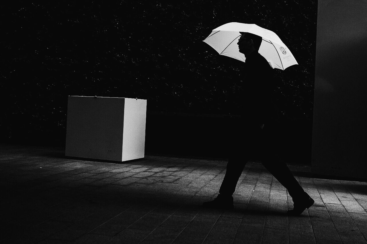 Full length of man with umbrella walking on street at night