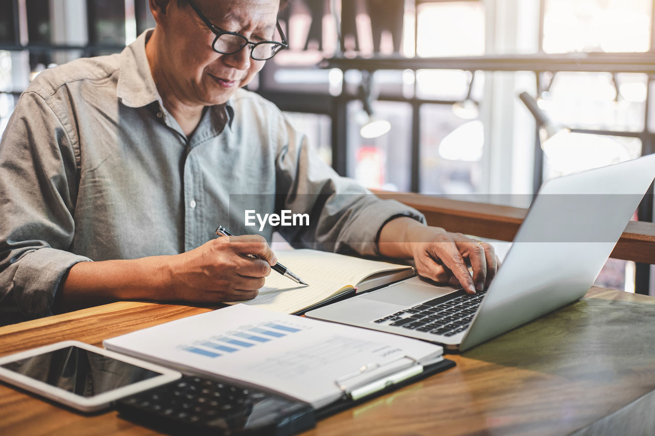 Midsection of businessman using laptop on desk in office