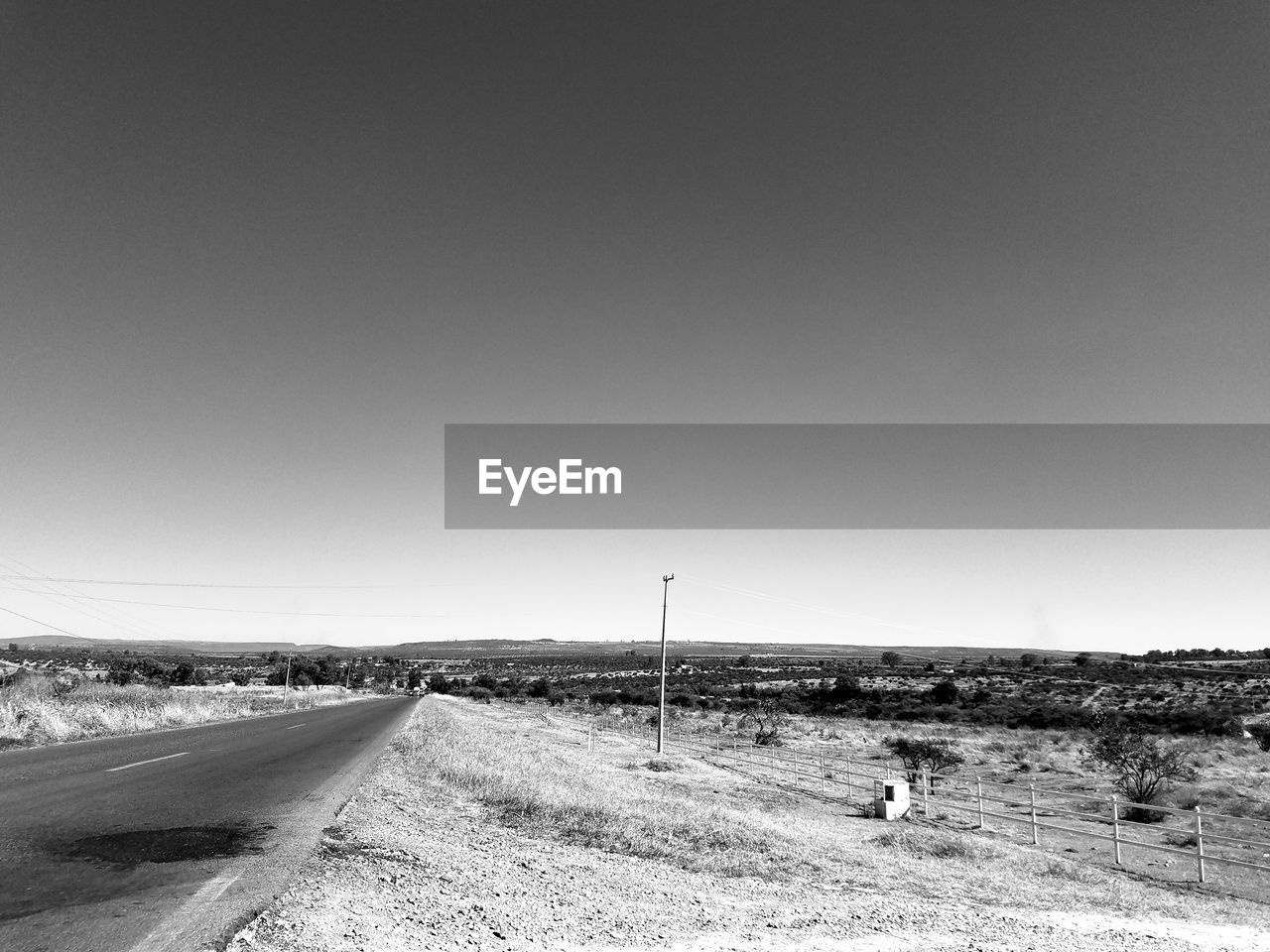 SCENIC VIEW OF ROAD BY FIELD AGAINST CLEAR SKY