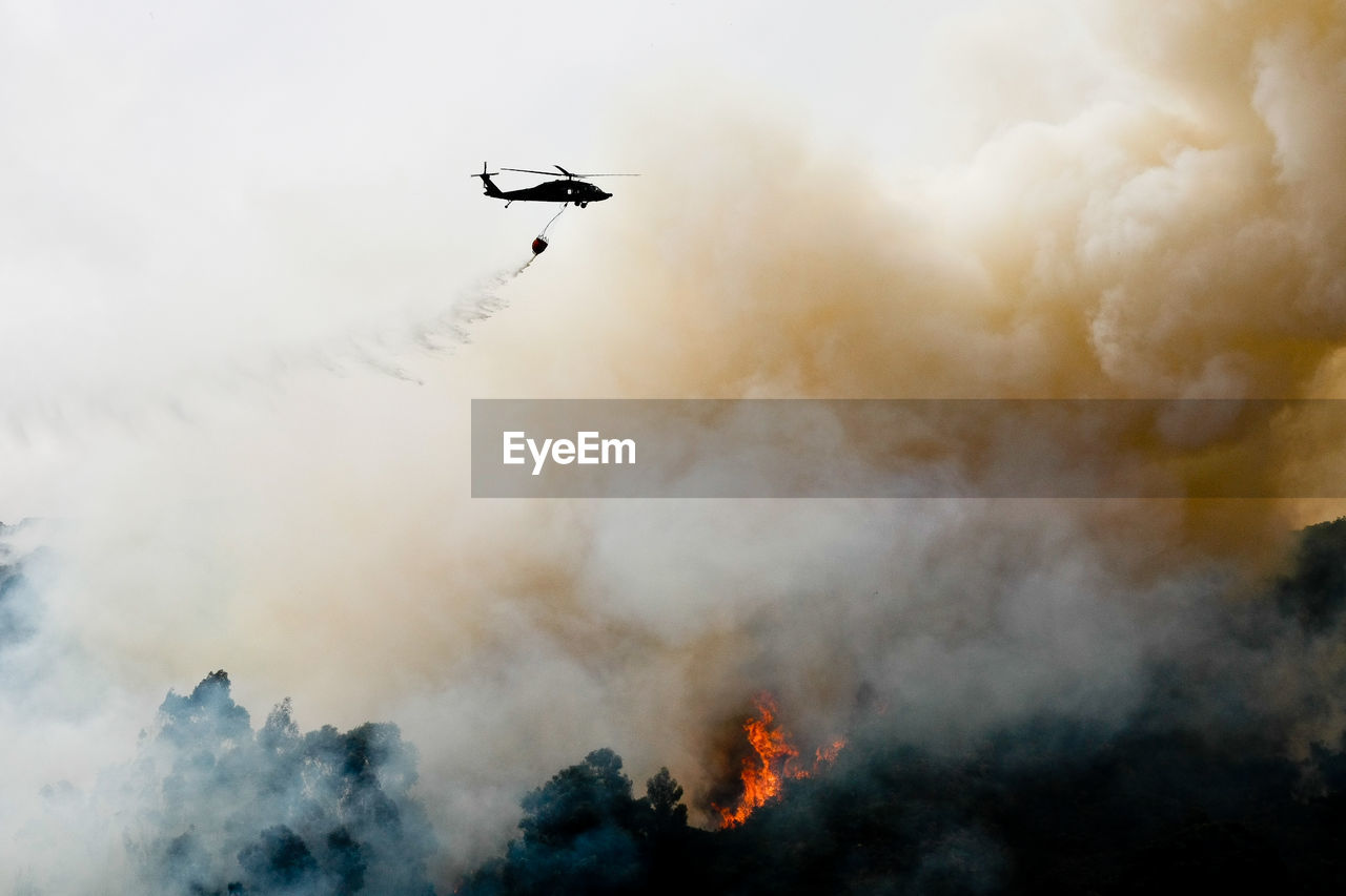 Silhouette helicopter extinguishing forest fire while flying over mountain