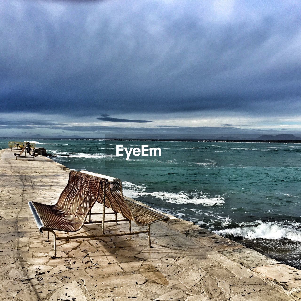 Benches at pier by sea against cloudy sky