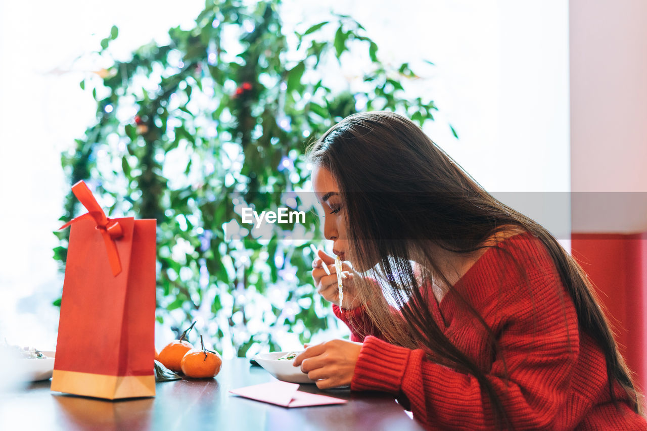 Beautiful smiling young asian woman in red clothes eating asian food in chinese  restaurant