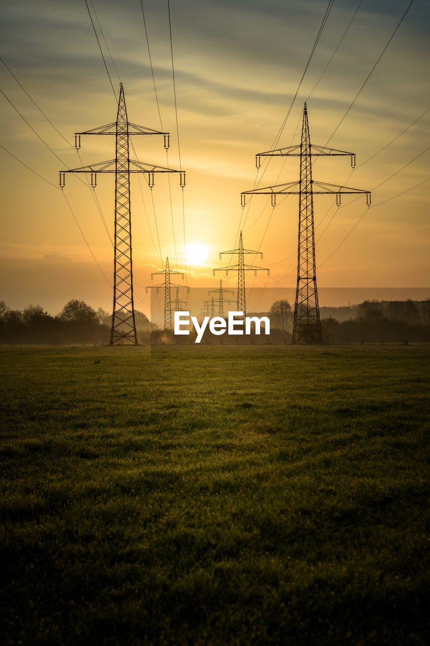 ELECTRICITY PYLONS ON FIELD AGAINST SKY DURING SUNSET
