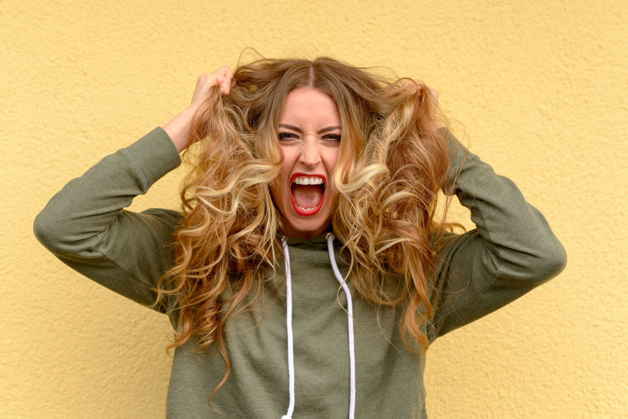 Angry woman tearing hair out against yellow wall