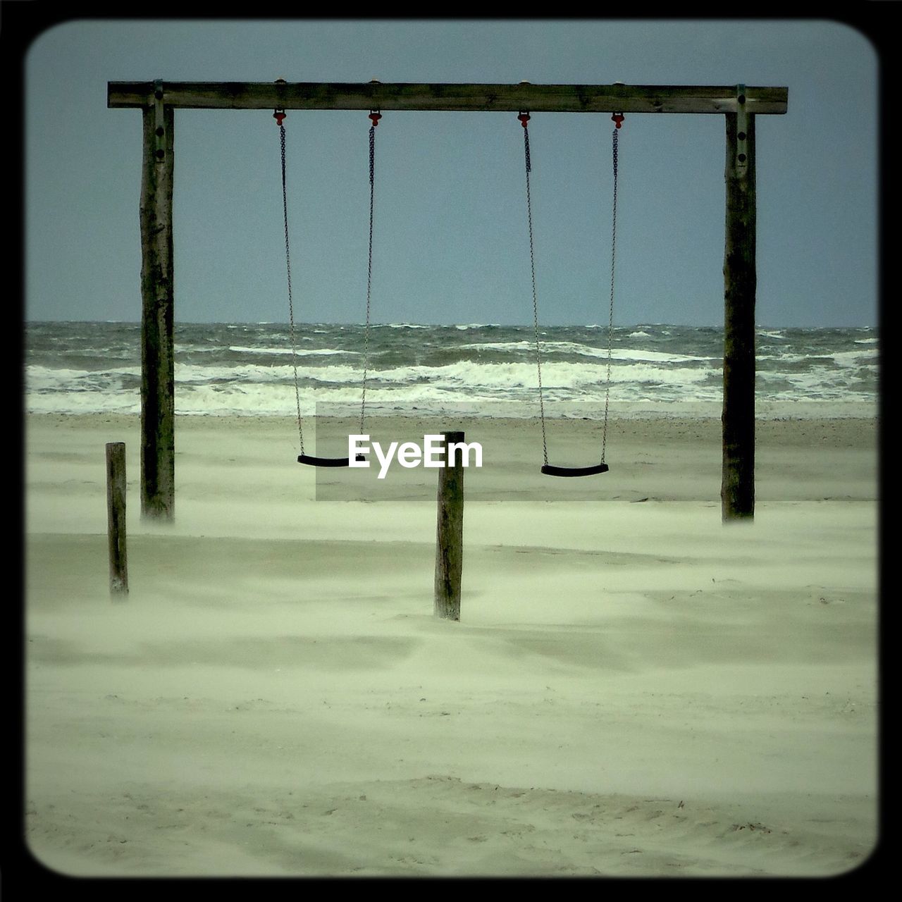 Empty swing on beach against clear sky
