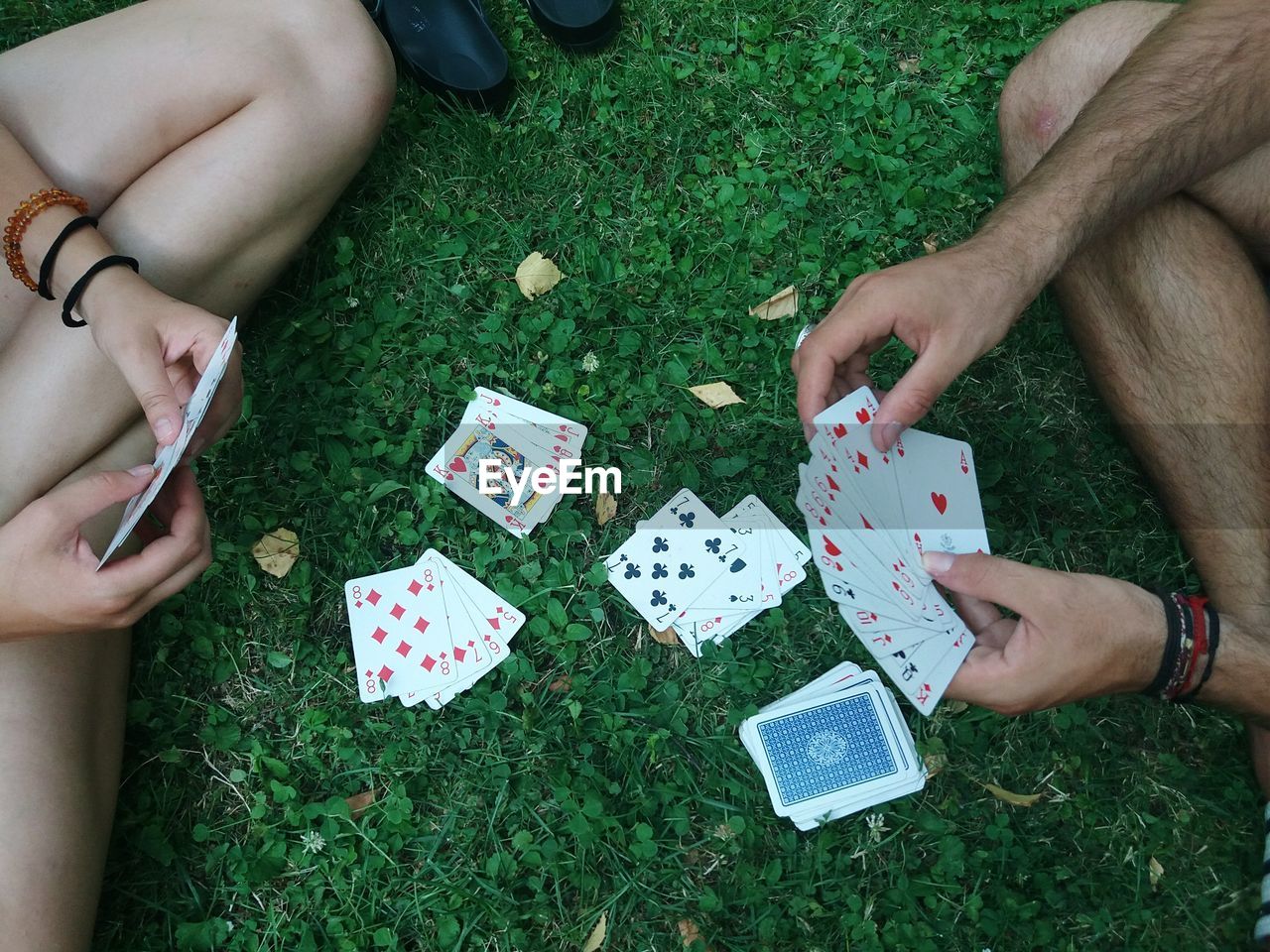 Low section of friends playing cards on grassy field 