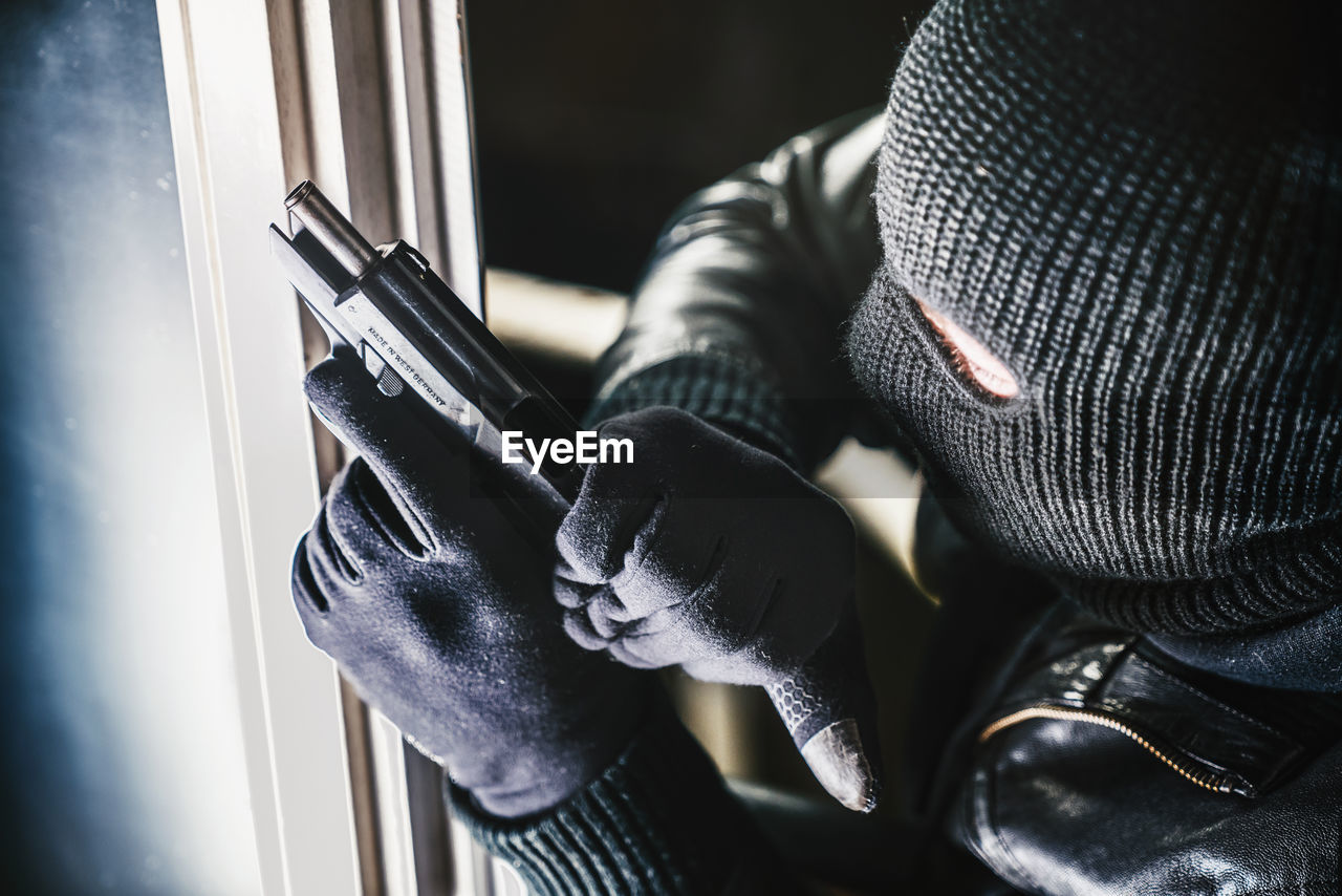 High angle view of burglar with gun standing by window
