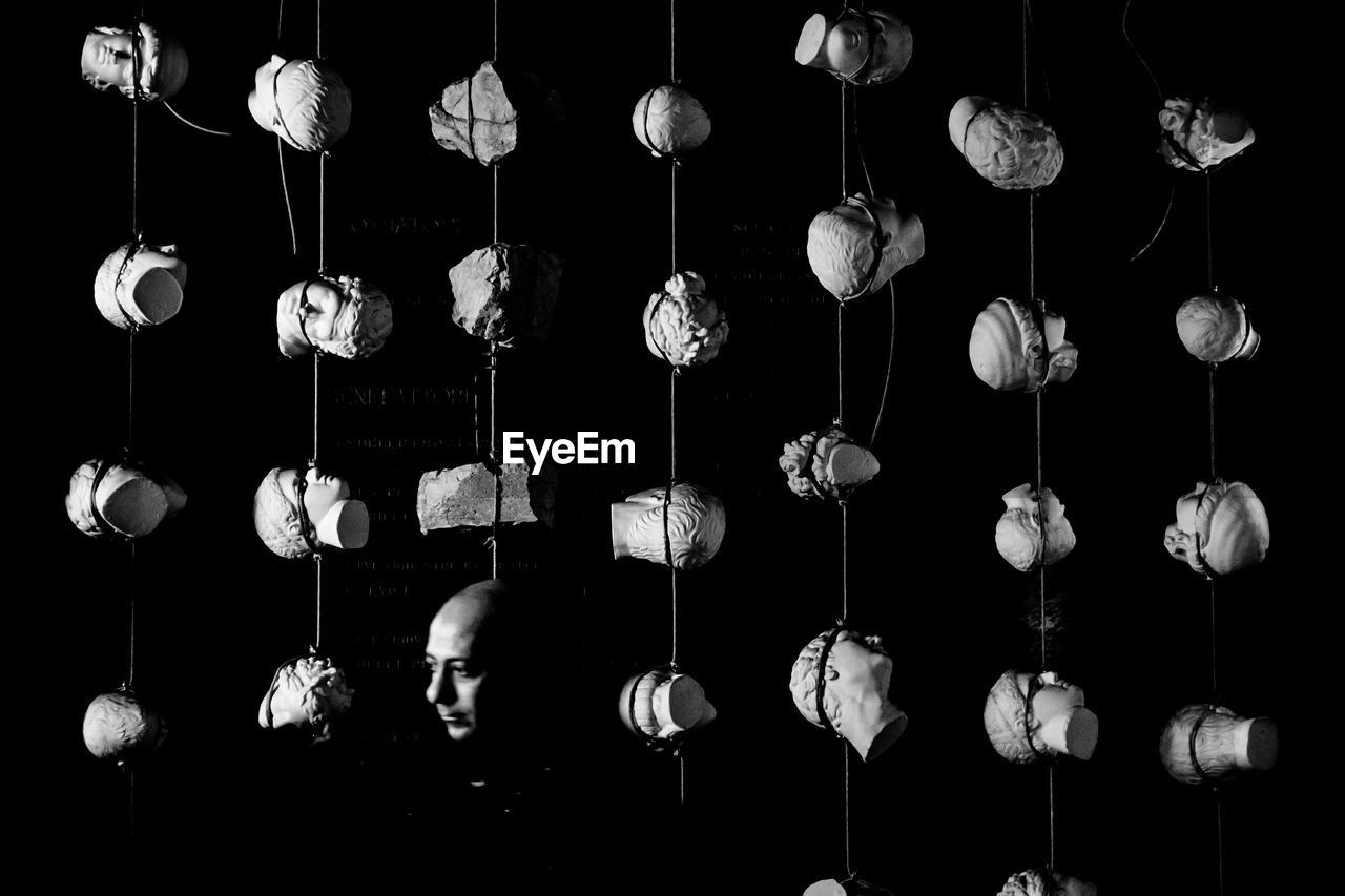 Man standing amidst mannequin heads hanging from ropes