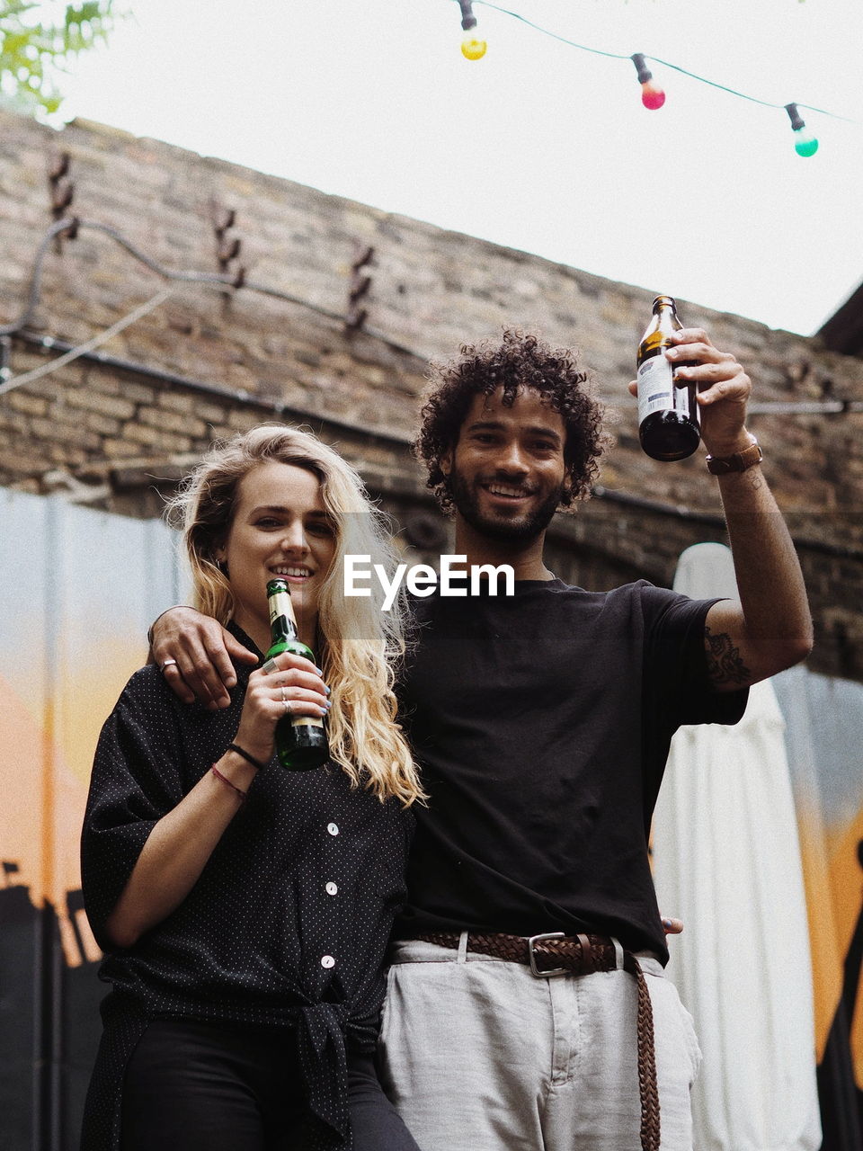 Low angle portrait of smiling friends holding alcoholic drink bottles