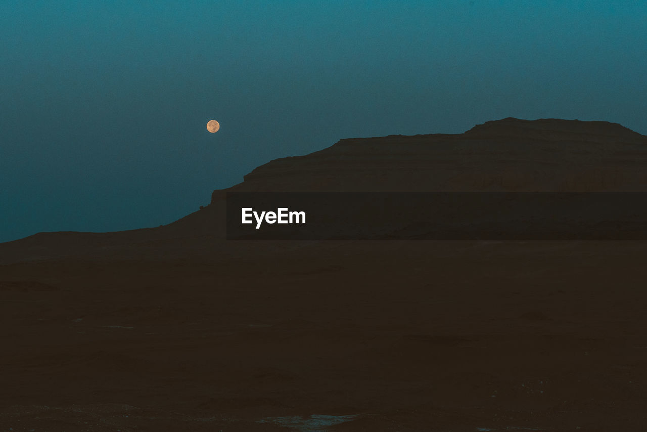 LOW ANGLE VIEW OF MOON ON MOUNTAIN AGAINST SKY