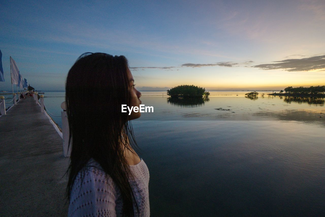 Woman looking at sea against sky during sunset