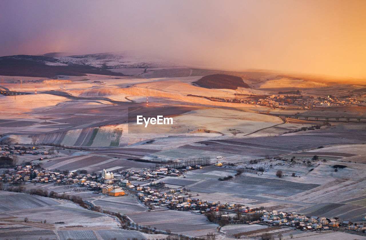 High angle view of snow covered landscape against sky during sunset
