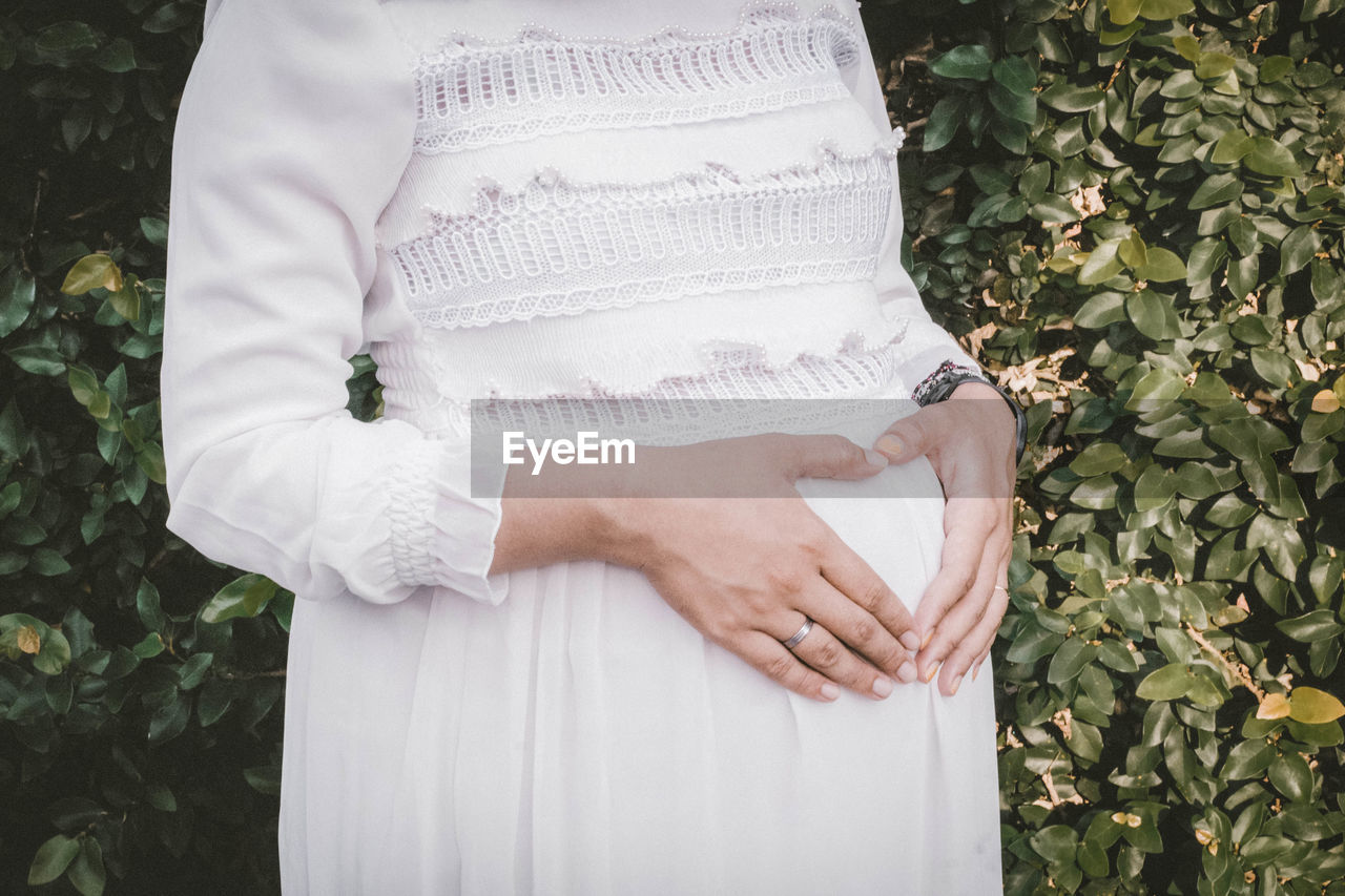 Midsection of pregnant woman standing by plants