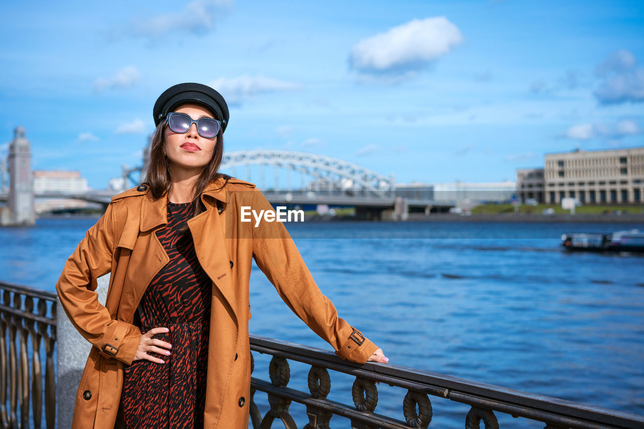 portrait of young woman wearing sunglasses standing against river