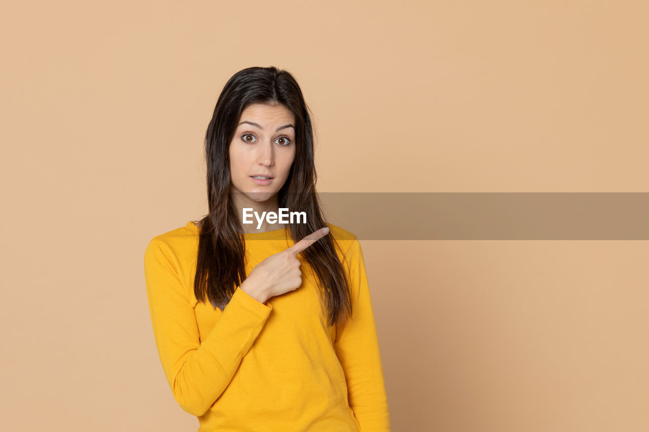 PORTRAIT OF A SERIOUS YOUNG WOMAN OVER YELLOW BACKGROUND