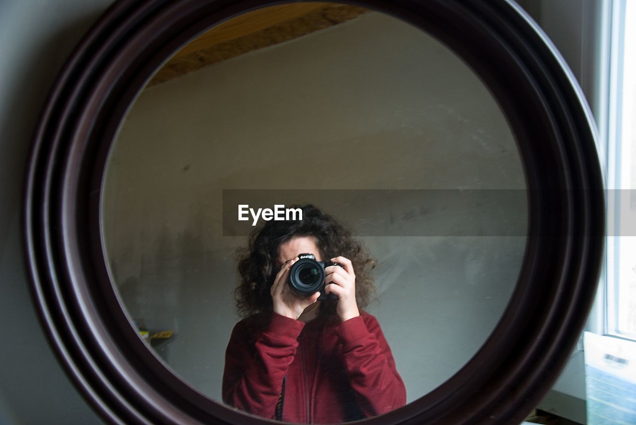 Portrait of woman photographing with camera seen on mirror