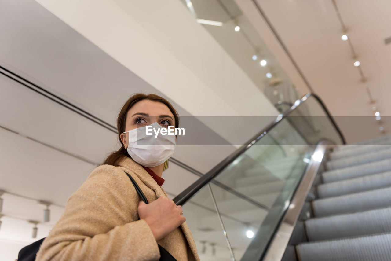 Low angle view of woman wearing mask sanding on escalator at shopping mall