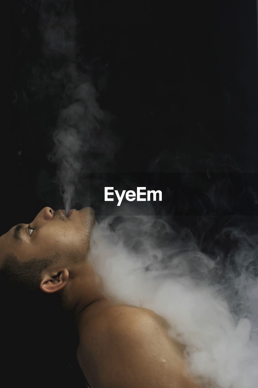 Side view man exhaling smoke over black background