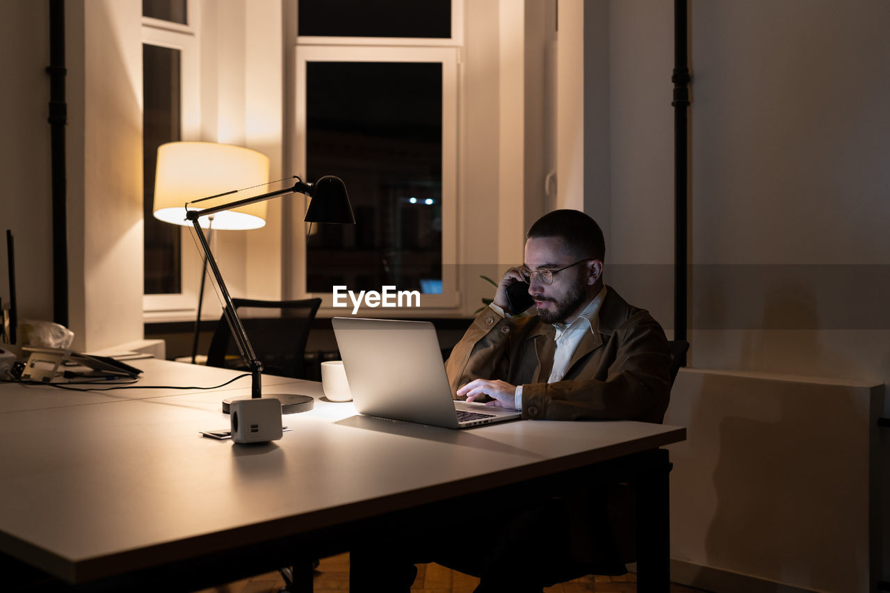 Young businessman, journalist or pr manager work at night on new project in empty coworking space
