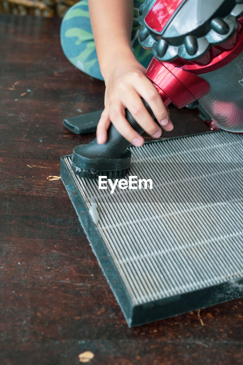 A young boy is cleaning the air filter sheet with the vacuum.