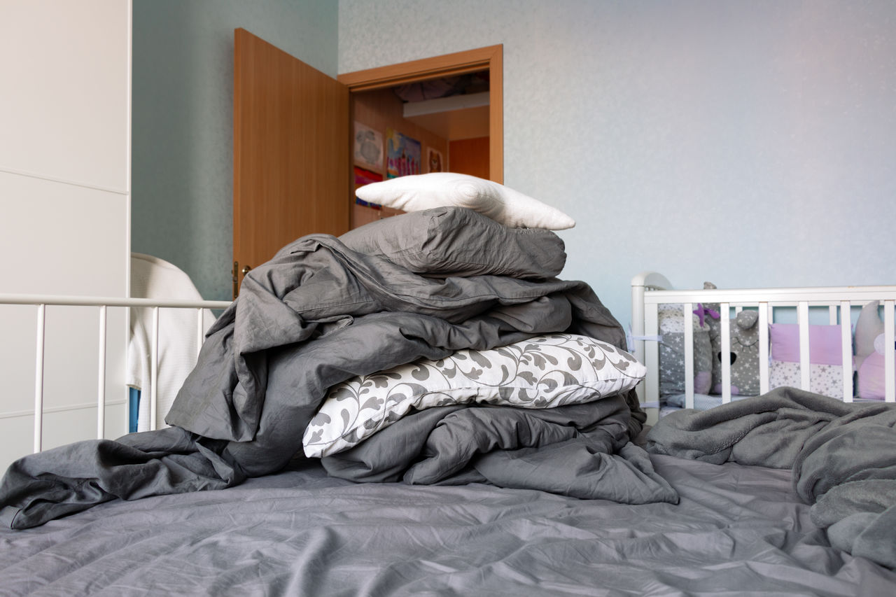 Big pile of gray linen and white pillows lies on bed in domestic room. housekeeping concept