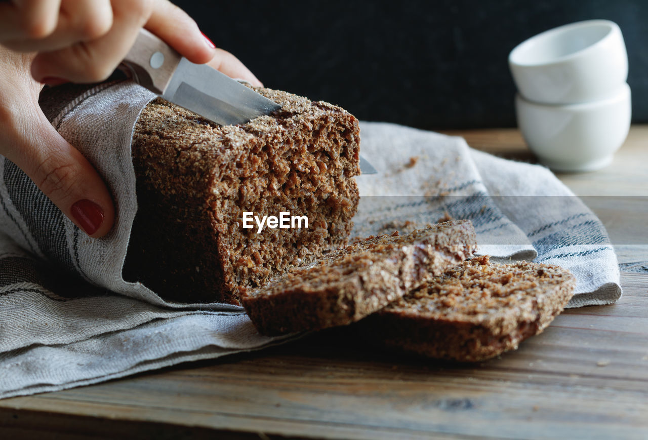 Cropped hand of woman cutting brown bread from knife