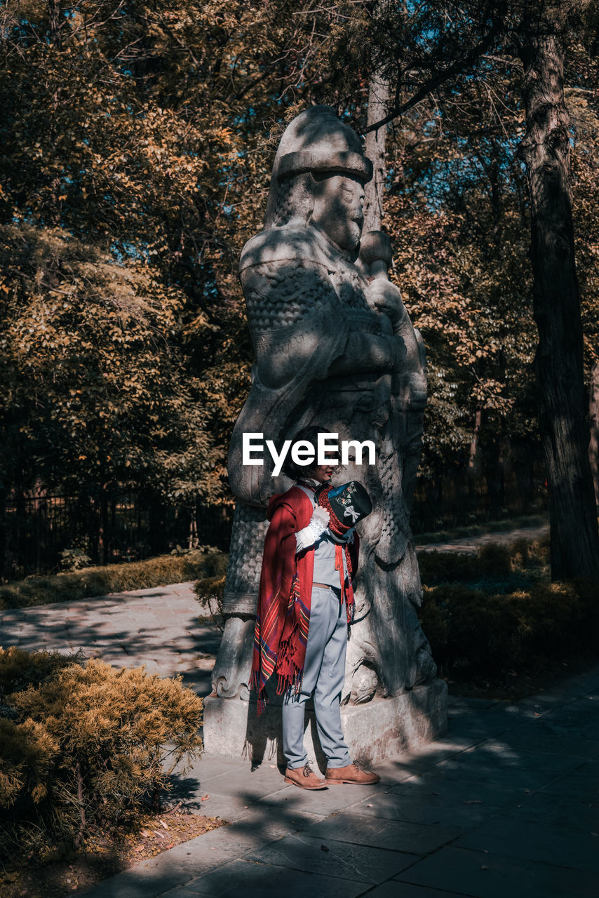 Man cosplaying mad hatter standing next to statue by trees