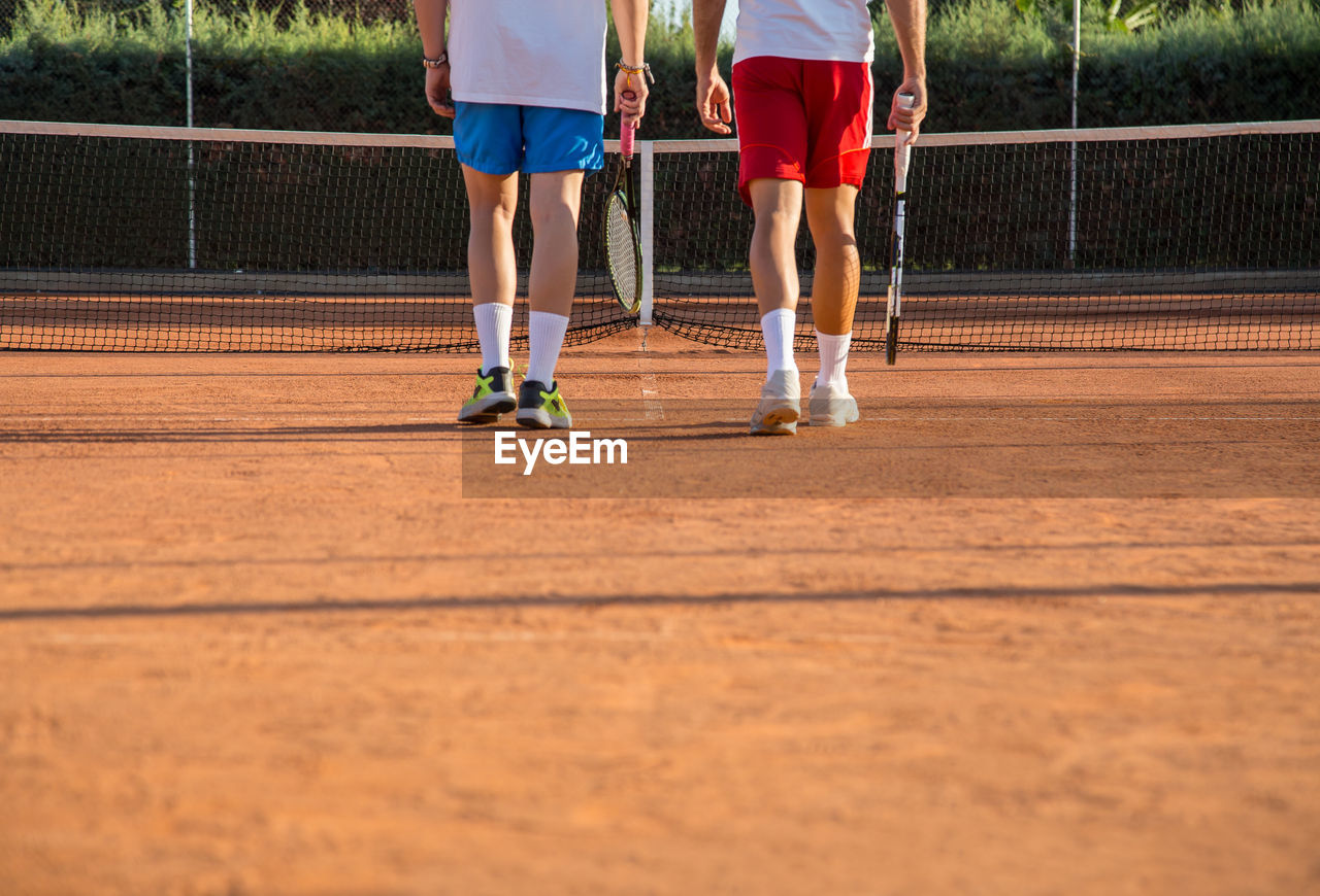 Low section of male friends playing tennis on court