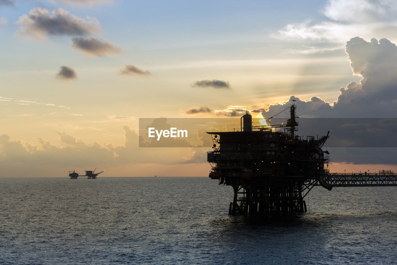 Seascape of oil field with silhouette of oil production platform during sunset at offshore oil field