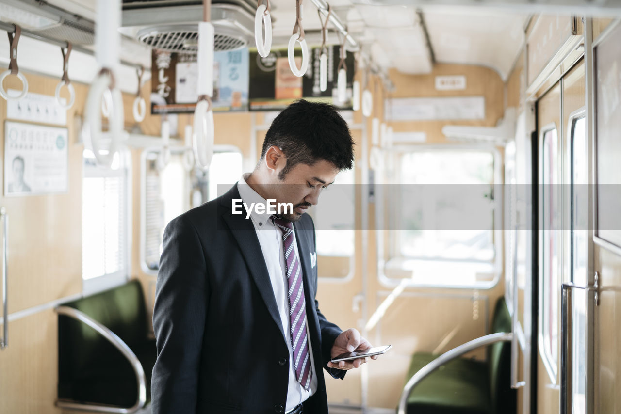 Businessman using smart phone while standing in train