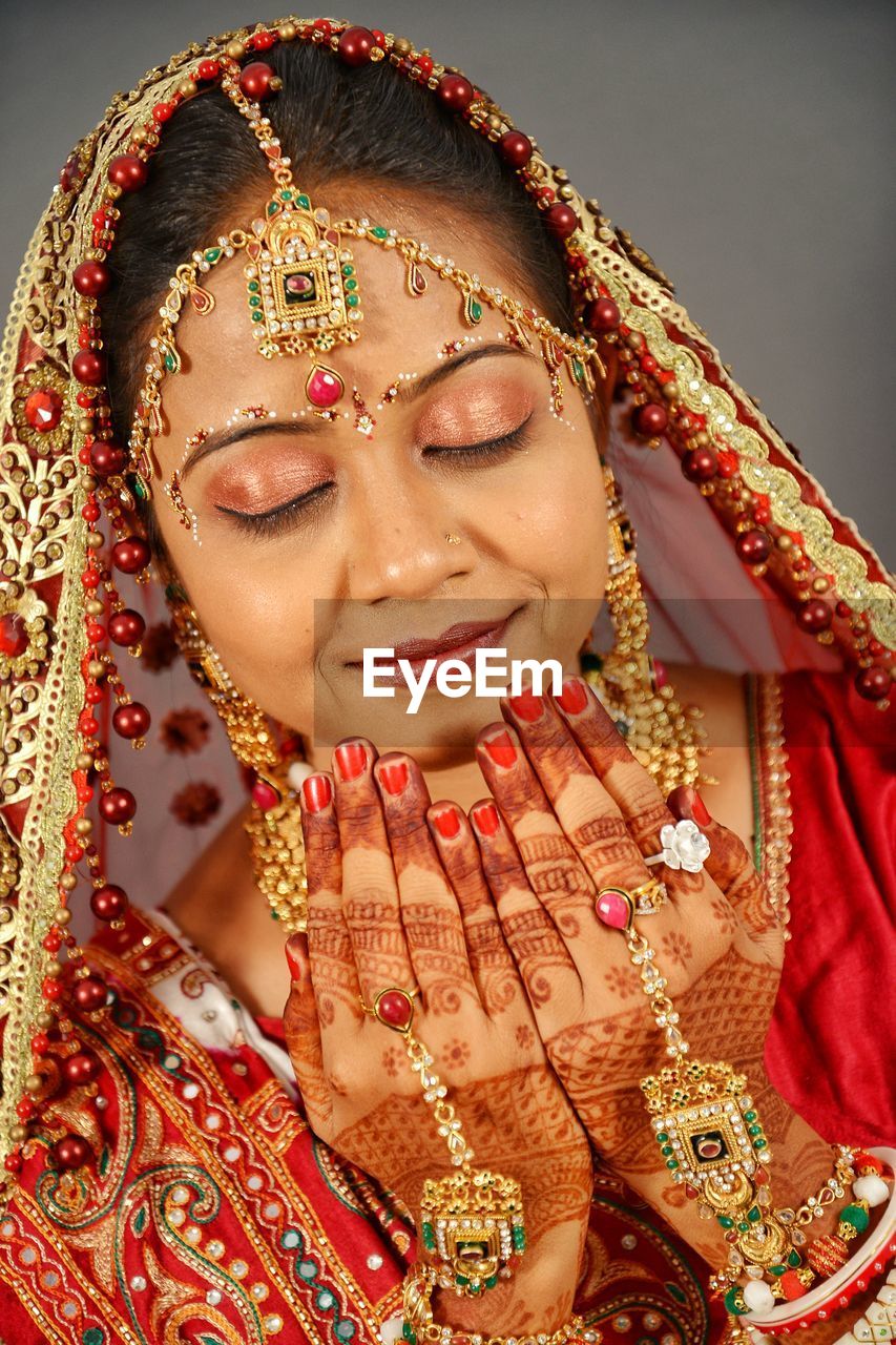 Close-up of smiling bride praying against wall at home